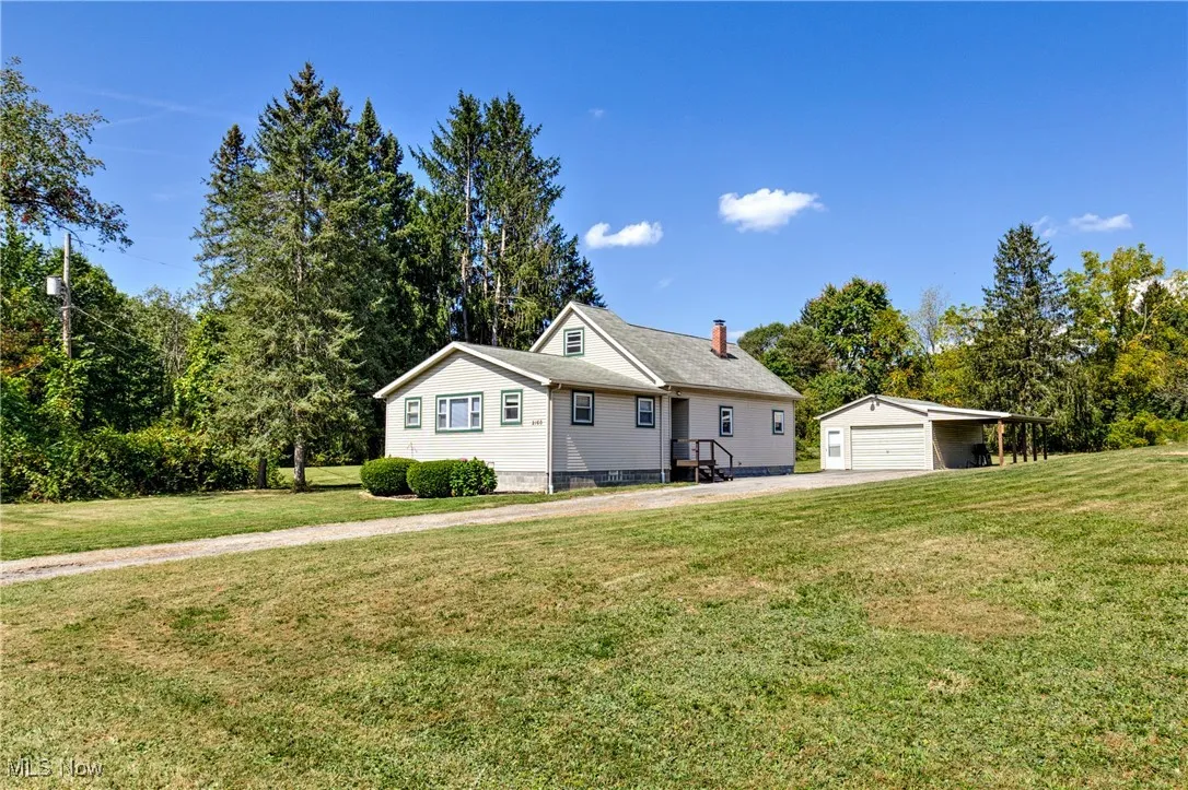 View of front facade featuring an outbuilding, a detached garage, a front lawn, and a chimney