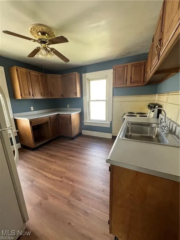 Kitchen featuring brown cabinets, white appliances, light countertops, and dark wood-type flooring