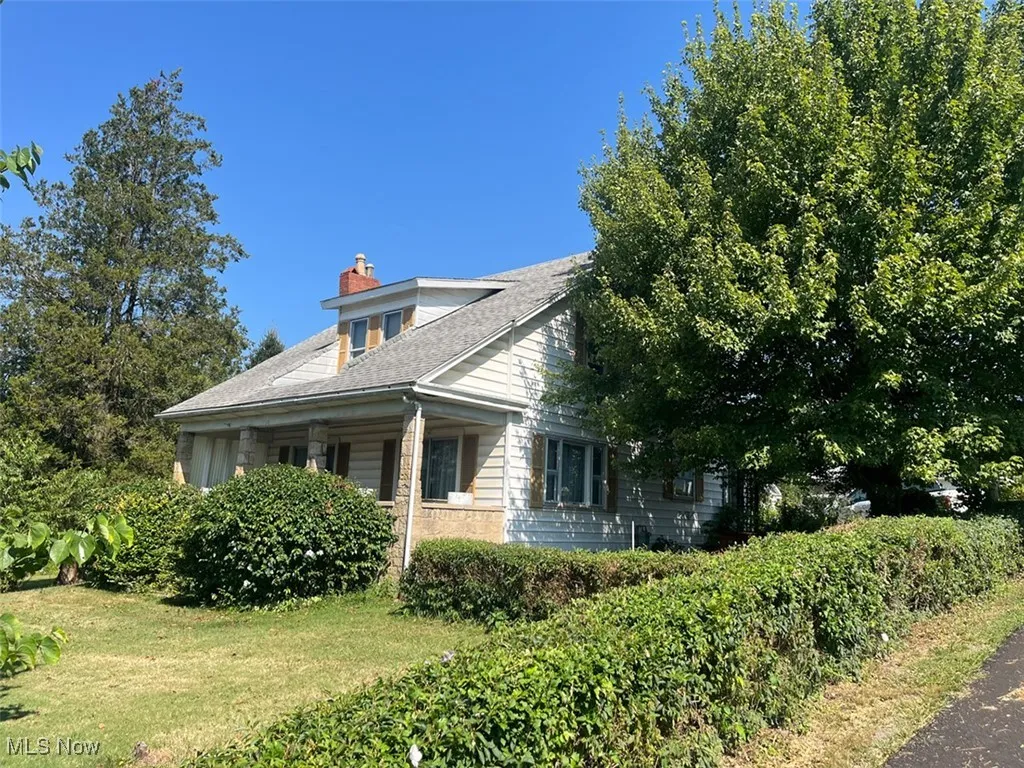 View of side of home with a chimney, covered porch, a yard, and roof with shingles