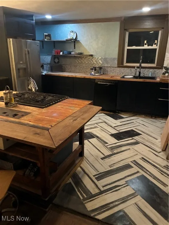 Kitchen with dark cabinetry, decorative backsplash, fridge, dishwashing machine, and stovetop
