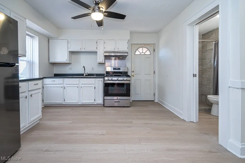 Kitchen featuring stainless steel appliances, dark countertops, white cabinets, and light wood-type flooring