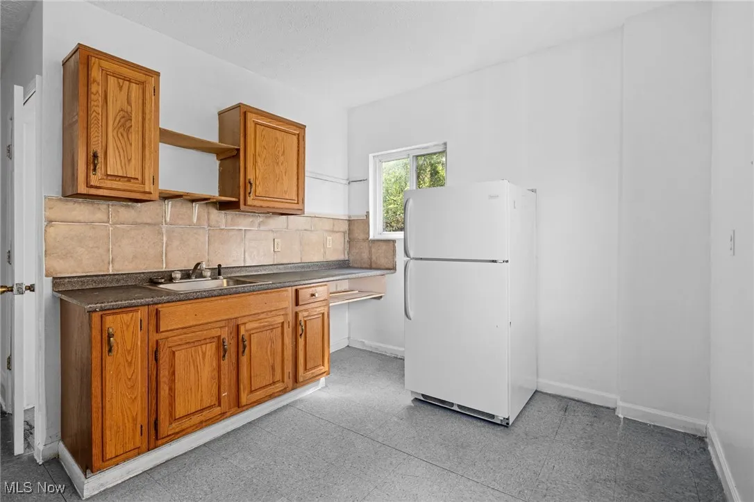 Kitchen with brown cabinets, freestanding refrigerator, dark countertops, open shelves, and tasteful backsplash