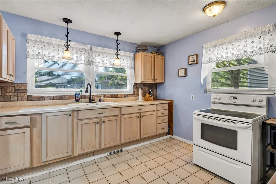 Kitchen with light brown cabinetry, white electric range, light countertops, and hanging light fixtures