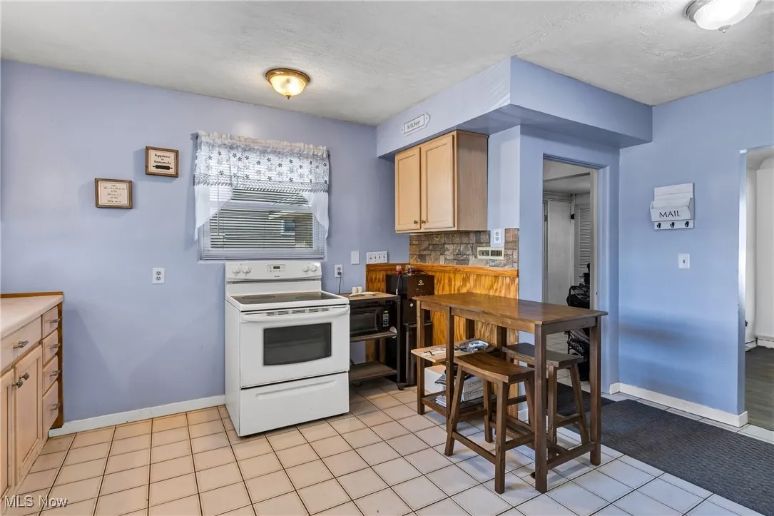 Kitchen featuring white electric range oven, light tile patterned flooring, light brown cabinetry, tasteful backsplash, and light countertops