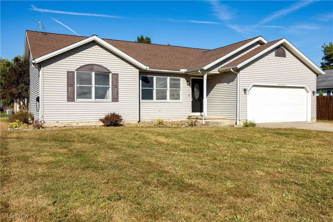 Single story home featuring a front yard, driveway, a shingled roof, and a garage