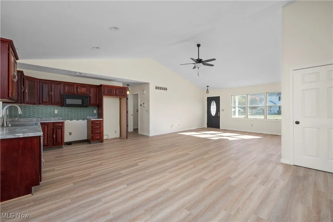 Kitchen with vaulted ceiling, light wood-style flooring, backsplash, black microwave, and reddish brown cabinets