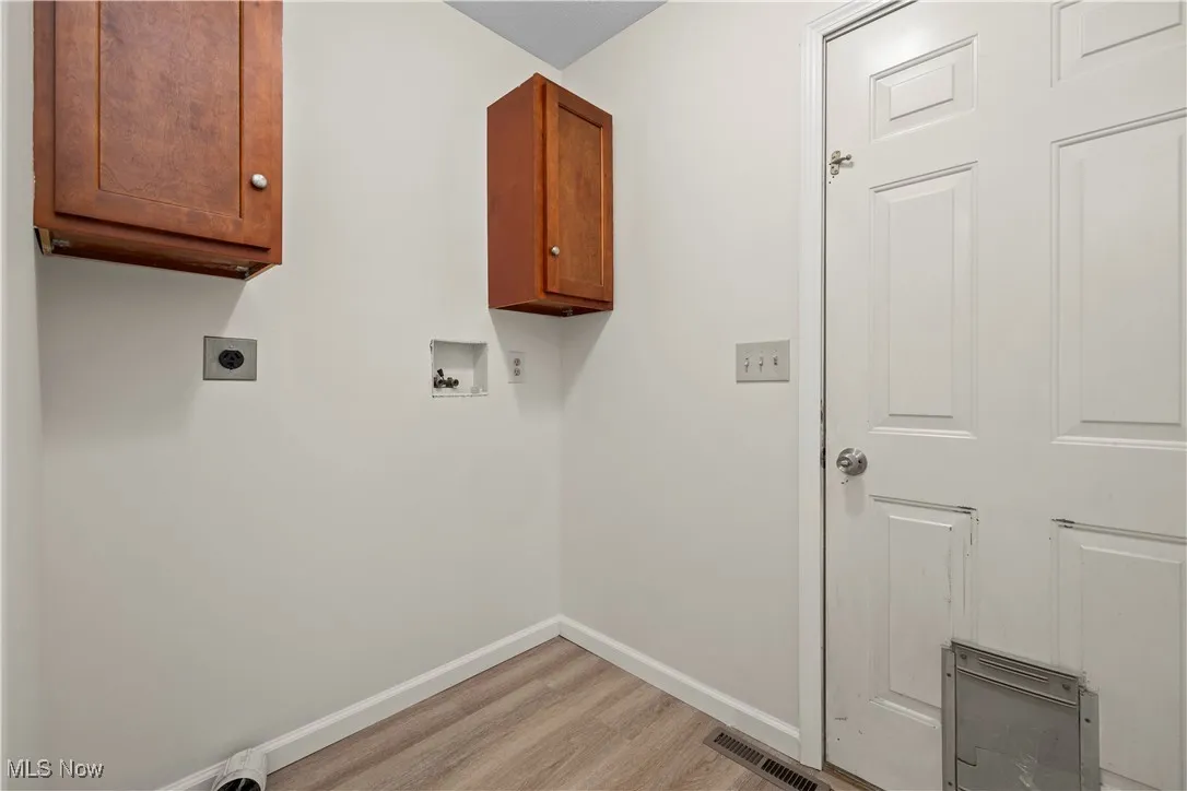 Washroom with electric dryer hookup, cabinet space, hookup for a washing machine, and light wood-style floors