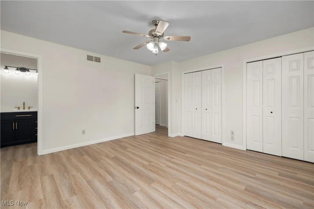 Unfurnished bedroom featuring multiple closets, light wood-style flooring, ensuite bathroom, and a ceiling fan