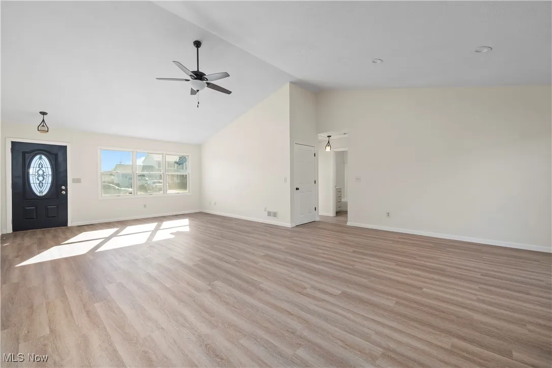 Unfurnished living room with high vaulted ceiling, light wood-style floors, and ceiling fan