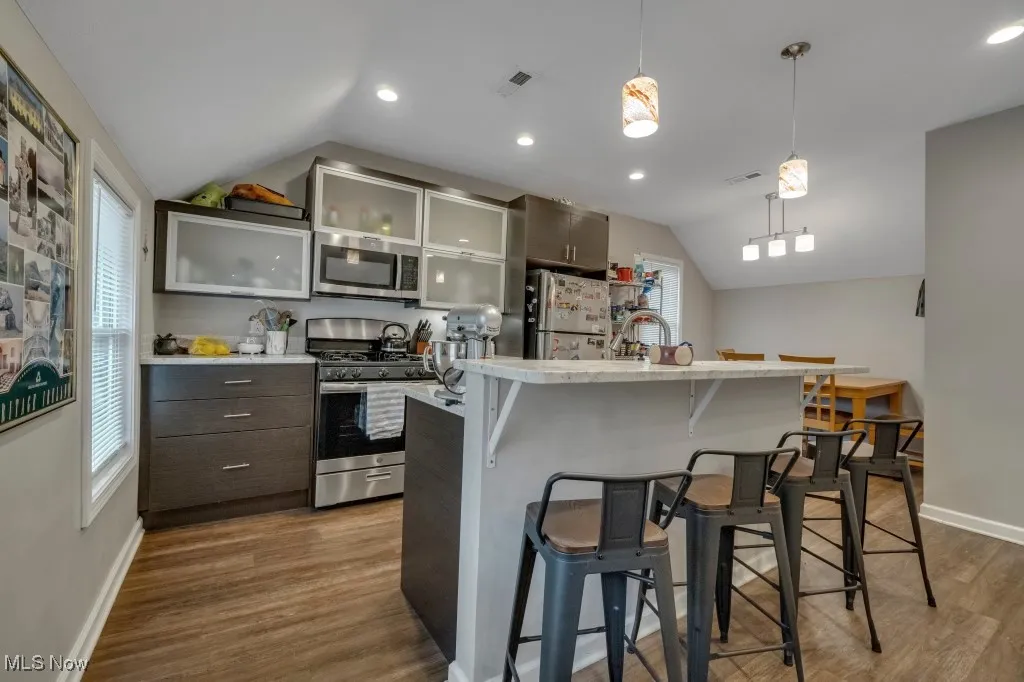 Kitchen with healthy amount of natural light, vaulted ceiling, stainless steel appliances, decorative light fixtures, and a kitchen breakfast bar