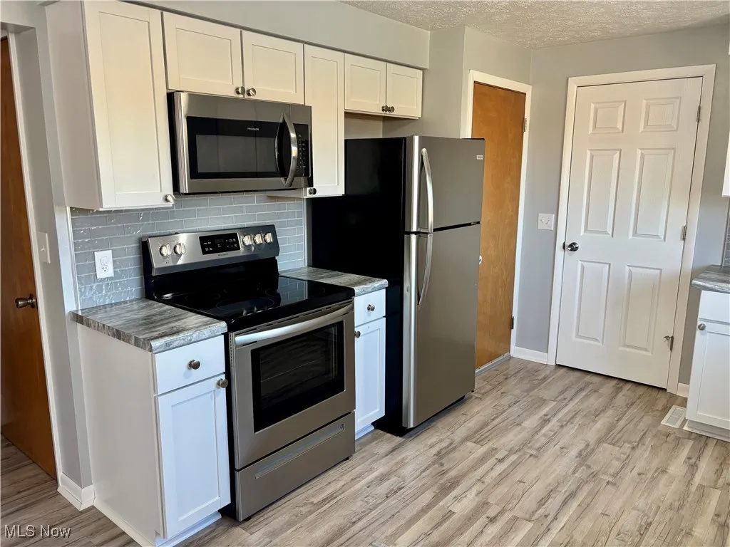 Kitchen featuring appliances with stainless steel finishes, white cabinets, decorative backsplash, light wood-style flooring, and a textured ceiling