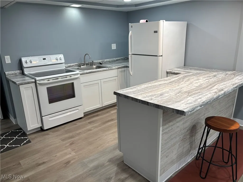 Kitchen with white appliances, a breakfast bar area, white cabinetry, light wood-style floors, and light countertops