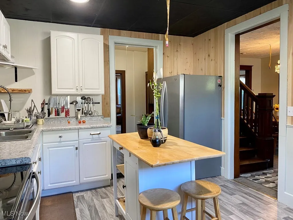 Kitchen with stainless steel appliances, butcher block countertops, light wood finished floors, white cabinetry, and wooden walls