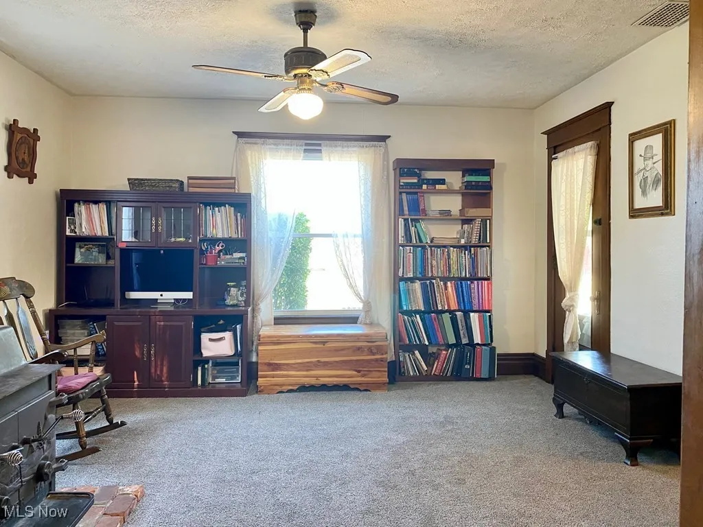 Sitting room with carpet floors, a ceiling fan, a textured ceiling, and a wood stove