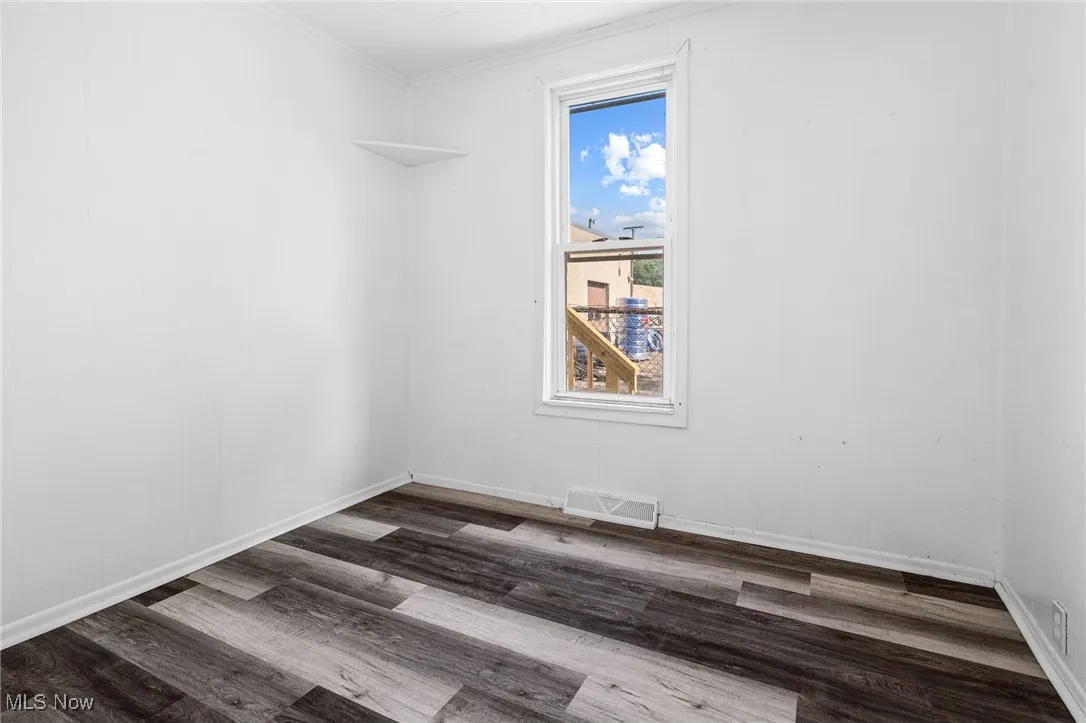 Empty room featuring dark wood-type flooring and crown molding