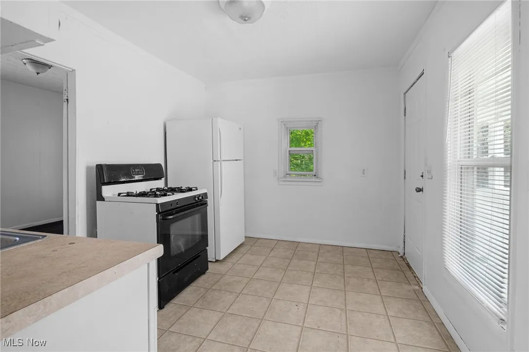Kitchen with black gas range, light countertops, ornamental molding, light tile patterned flooring, and freestanding refrigerator