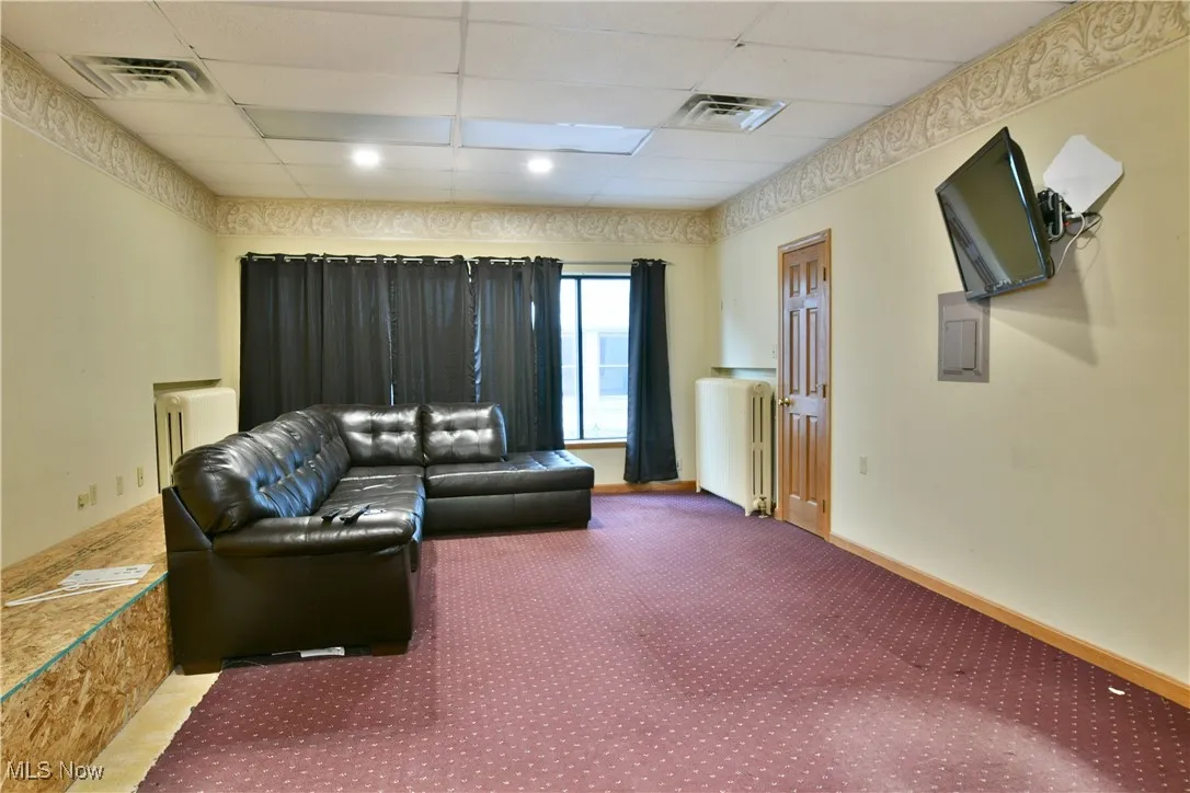 Carpeted living area featuring a drop ceiling and radiator heating unit
