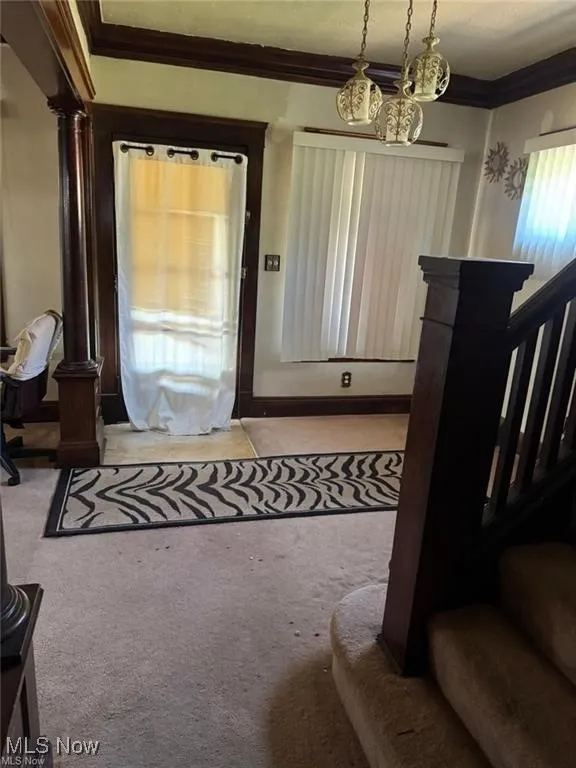 Foyer with ornamental molding, light carpet, stairs, and decorative columns