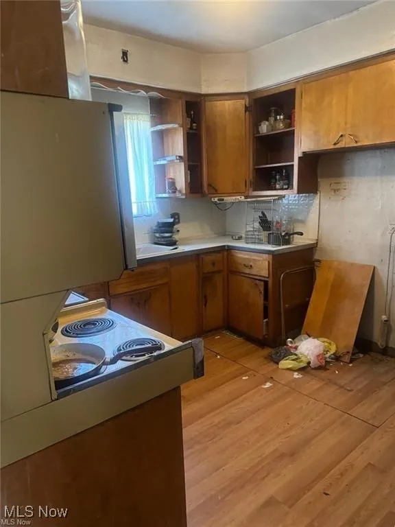 Kitchen featuring brown cabinetry, backsplash, light wood-style flooring, light countertops, and white electric range