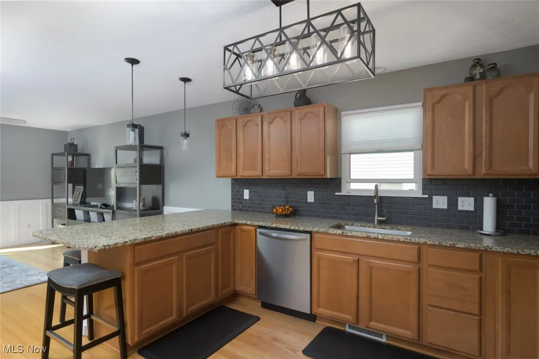 Kitchen with light stone counters, a peninsula, hanging light fixtures, a breakfast bar area, and stainless steel dishwasher