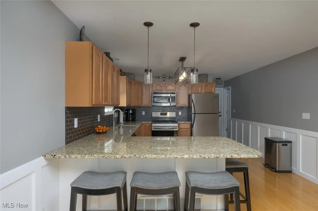Kitchen featuring a decorative wall, wainscoting, a peninsula, a breakfast bar, and stainless steel appliances
