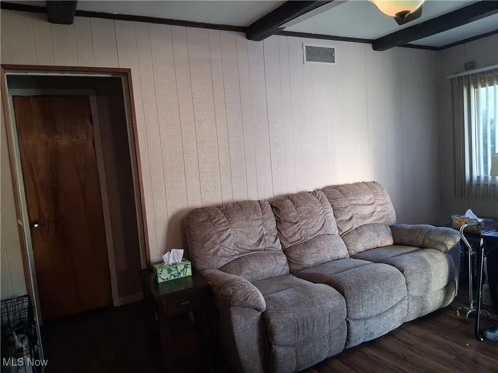 Living room with wood finished floors, beamed ceiling, and wooden walls