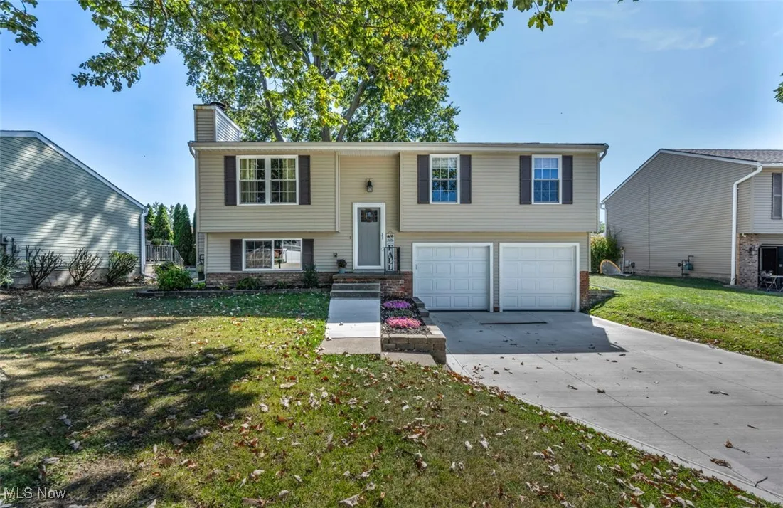 Raised ranch with a chimney, concrete driveway, a front lawn, brick siding, and a garage