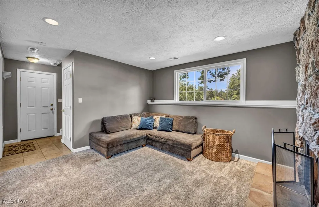 Living room with light colored carpet, a textured ceiling, light tile patterned floors, and recessed lighting