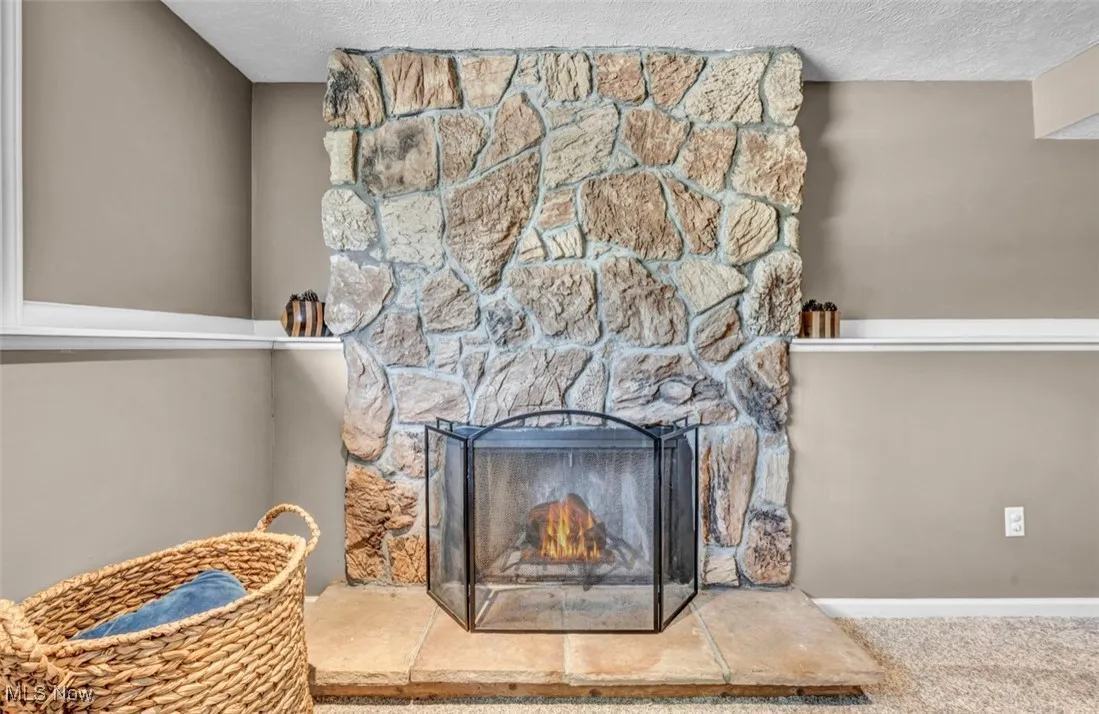 Detailed view of a stone fireplace, a textured ceiling, and carpet floors