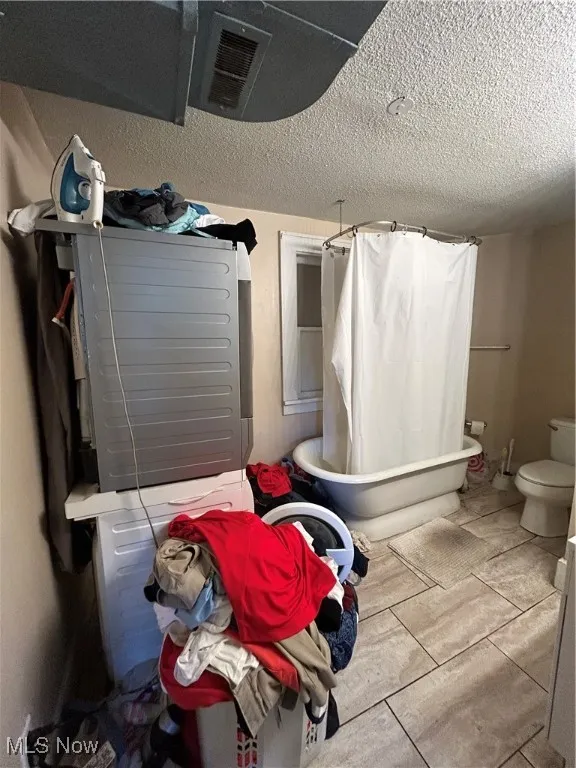 Full bath featuring a textured ceiling and a combined bath / shower with freestanding tub