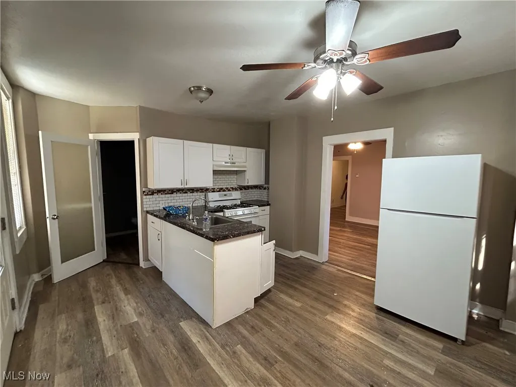 Kitchen with backsplash, white appliances, white cabinetry, dark wood finished floors, and dark stone counters