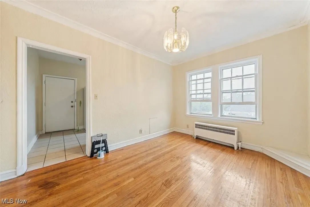 Spare room featuring radiator, light wood-style floors, ornamental molding, and a chandelier
