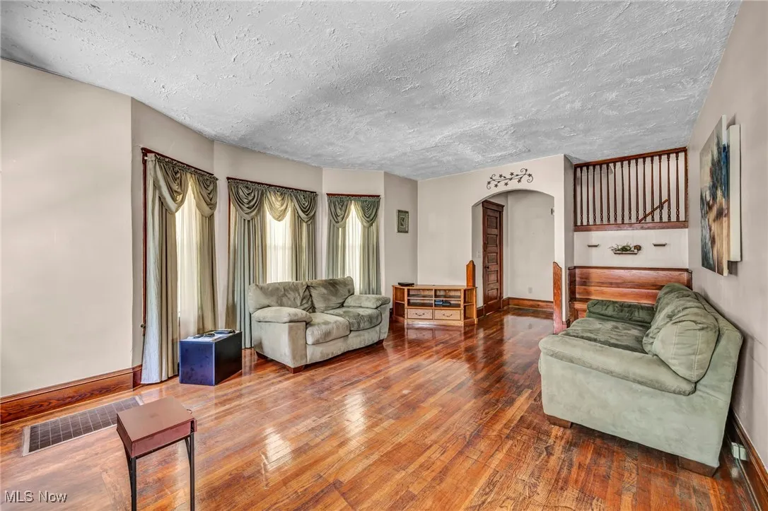 Living area featuring arched walkways, wood finished floors, a textured ceiling, and stairs