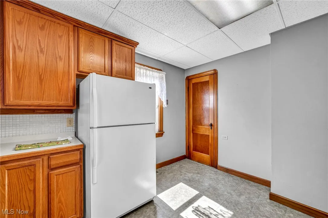 Kitchen featuring light countertops, brown cabinets, freestanding refrigerator, a paneled ceiling, and decorative backsplash