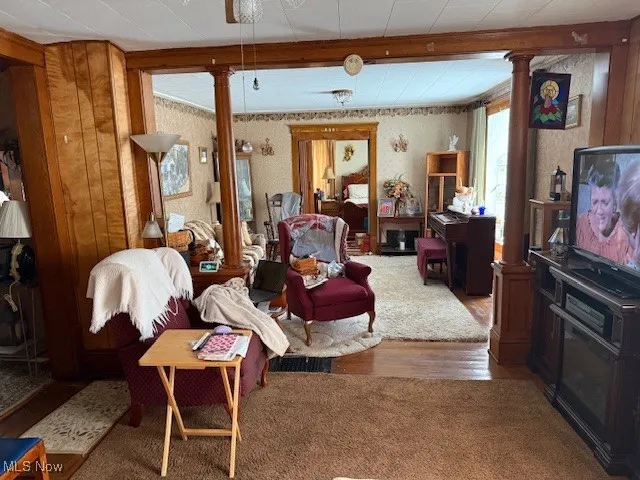 Living room with wood finished floors, decorative columns, beam ceiling, and ceiling fan