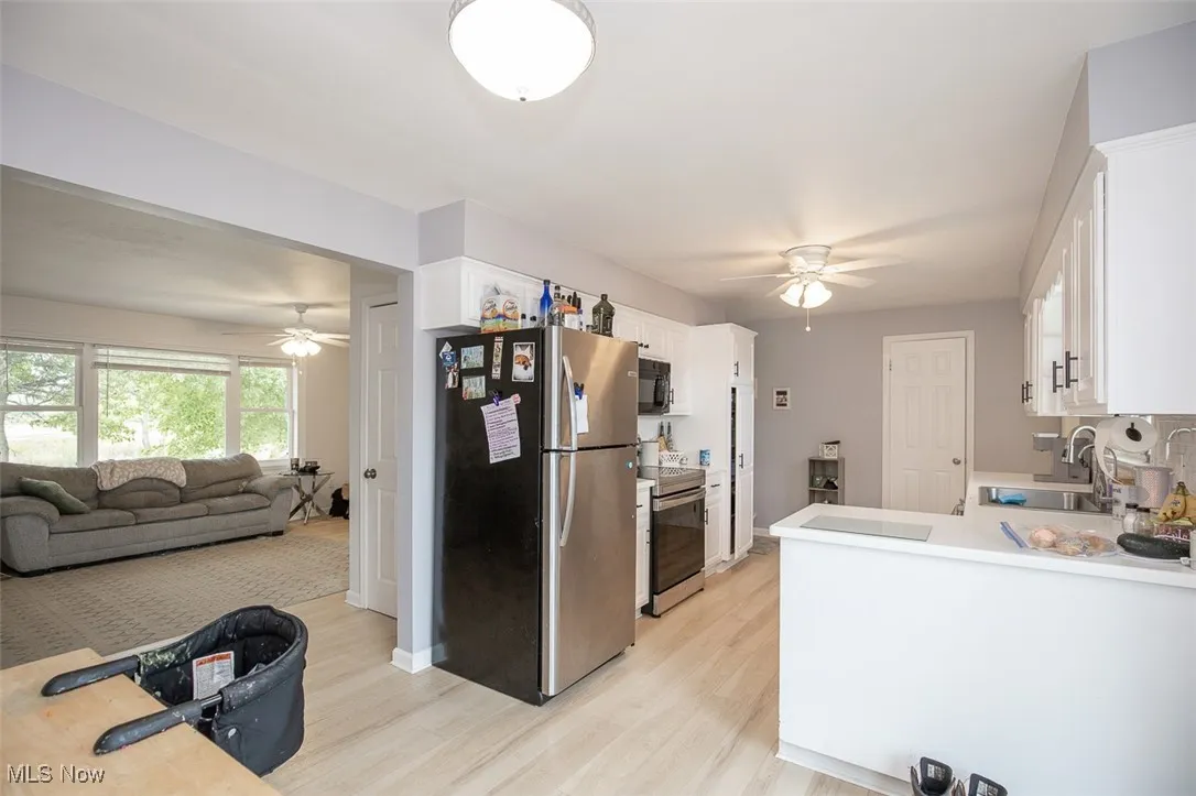 Kitchen with a ceiling fan, white cabinets, appliances with stainless steel finishes, light countertops, and light wood-style floors