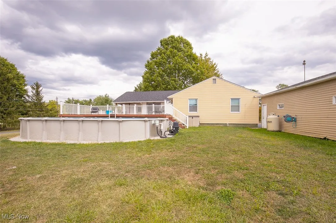 Back of house with an outdoor pool, a deck, and a yard