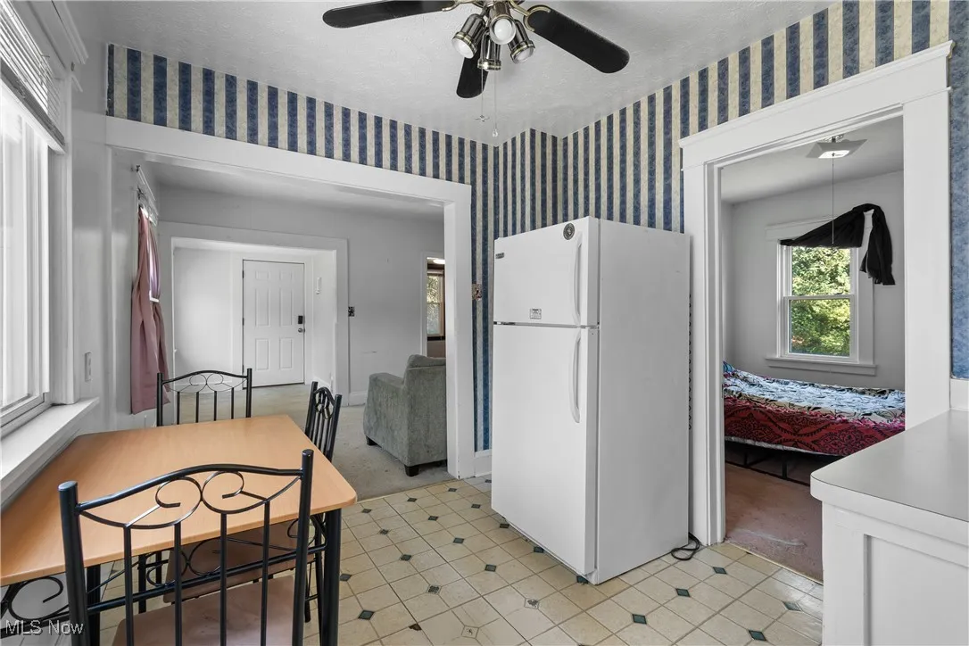 Kitchen with freestanding refrigerator, wallpapered walls, light colored carpet, and a ceiling fan