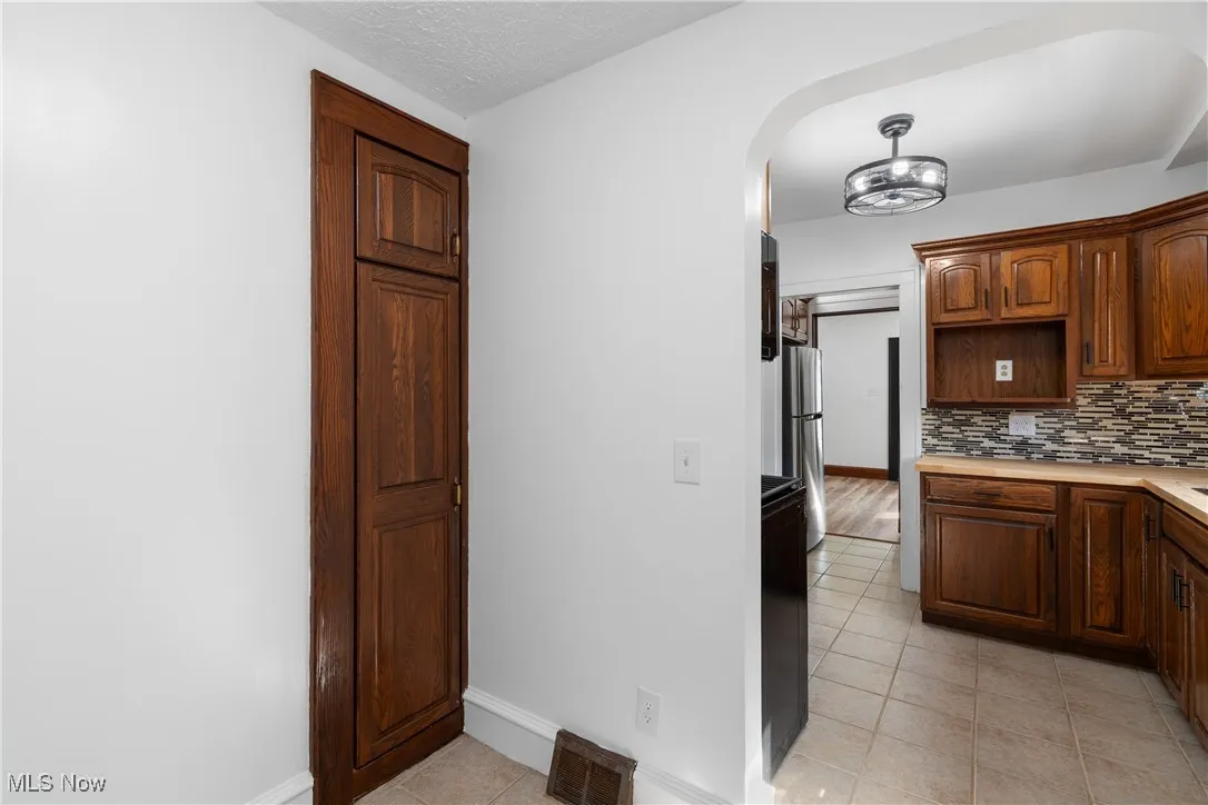 Kitchen featuring light tile patterned floors, light countertops, tasteful backsplash, freestanding refrigerator, and arched walkways