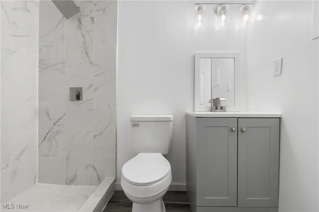 Full bathroom featuring vanity, a marble finish shower, and dark wood-type flooring