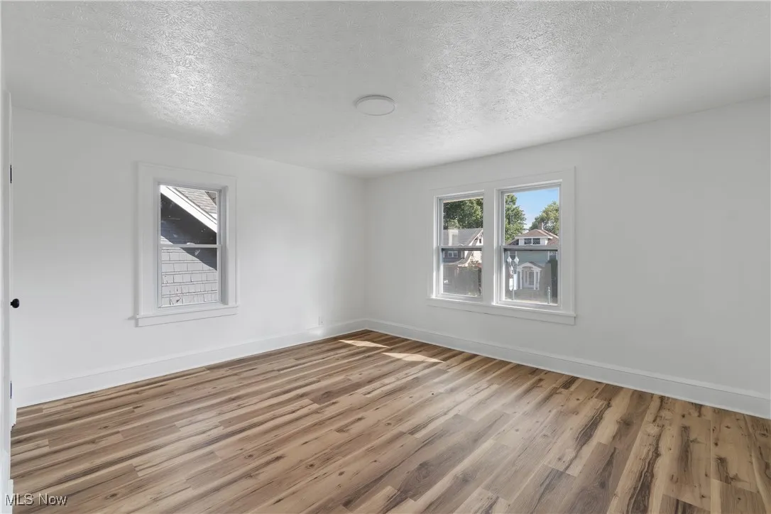 Spare room with a textured ceiling, light wood-type flooring, and healthy amount of natural light