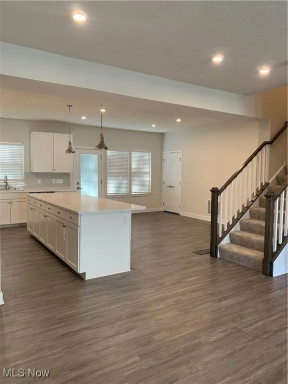 Kitchen featuring open floor plan, hanging light fixtures, dark wood-style floors, white cabinetry, and a center island