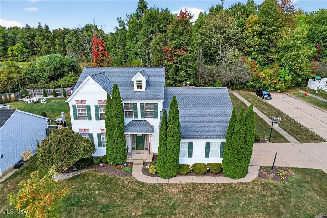 Traditional-style home with a front yard, a shingled roof, and a view of trees