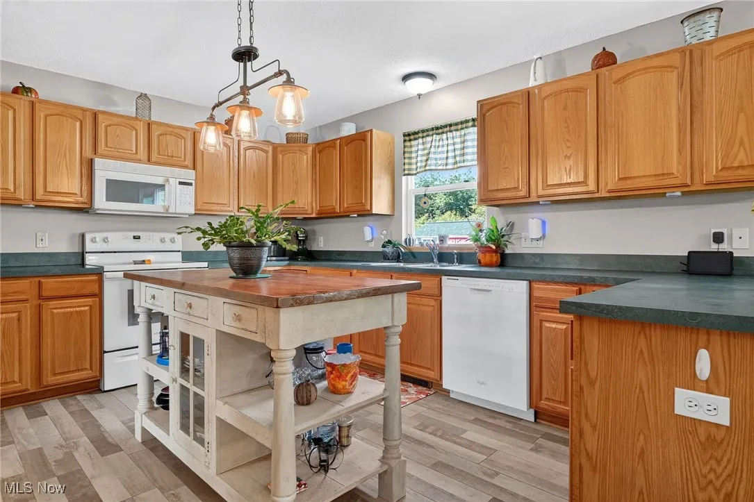 Kitchen with dark countertops, white appliances, pendant lighting, and light wood-style floors