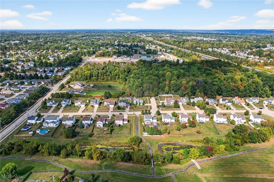 Aerial view of property and surrounding area featuring nearby suburban area and a tree filled landscape