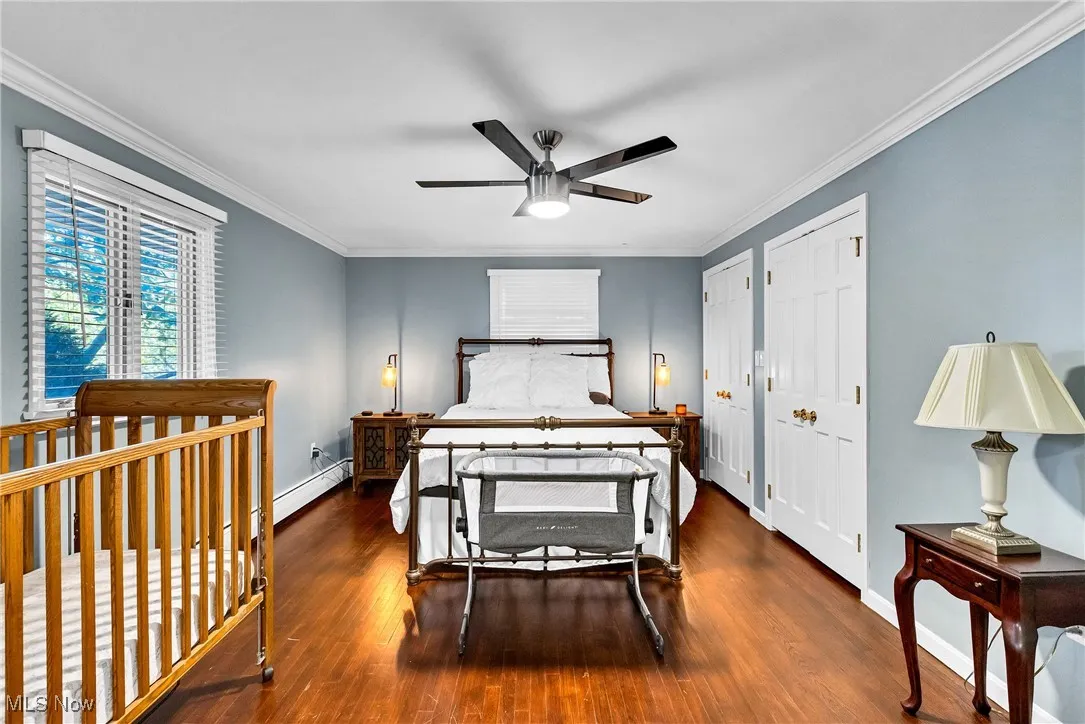 Bedroom featuring crown molding, wood finished floors, ceiling fan, and multiple closets