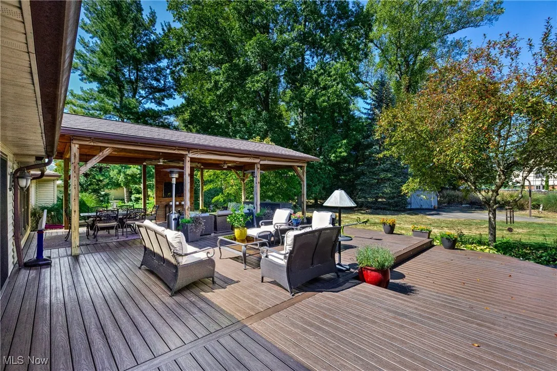 Wooden terrace with an outdoor living space, outdoor dining area, view of wooded area, and a storage unit