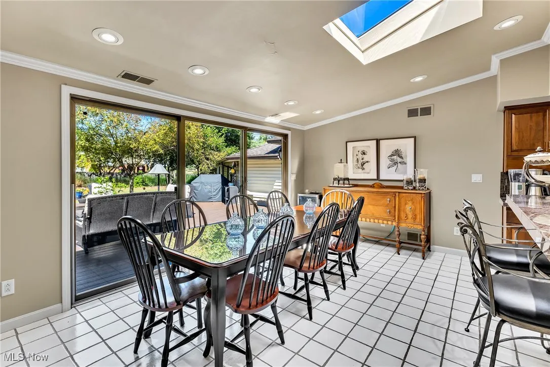 Dining space with crown molding, a skylight, vaulted ceiling, light tile patterned floors, and recessed lighting