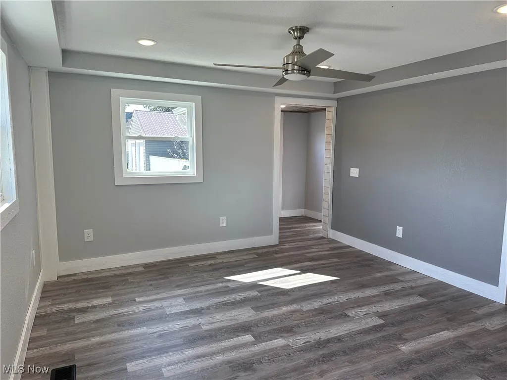 Spare room featuring dark wood-style flooring, recessed lighting, a ceiling fan, and a tray ceiling