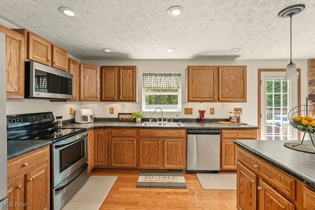 Kitchen featuring stainless steel appliances, dark countertops, light wood-style flooring, brown cabinets, and recessed lighting